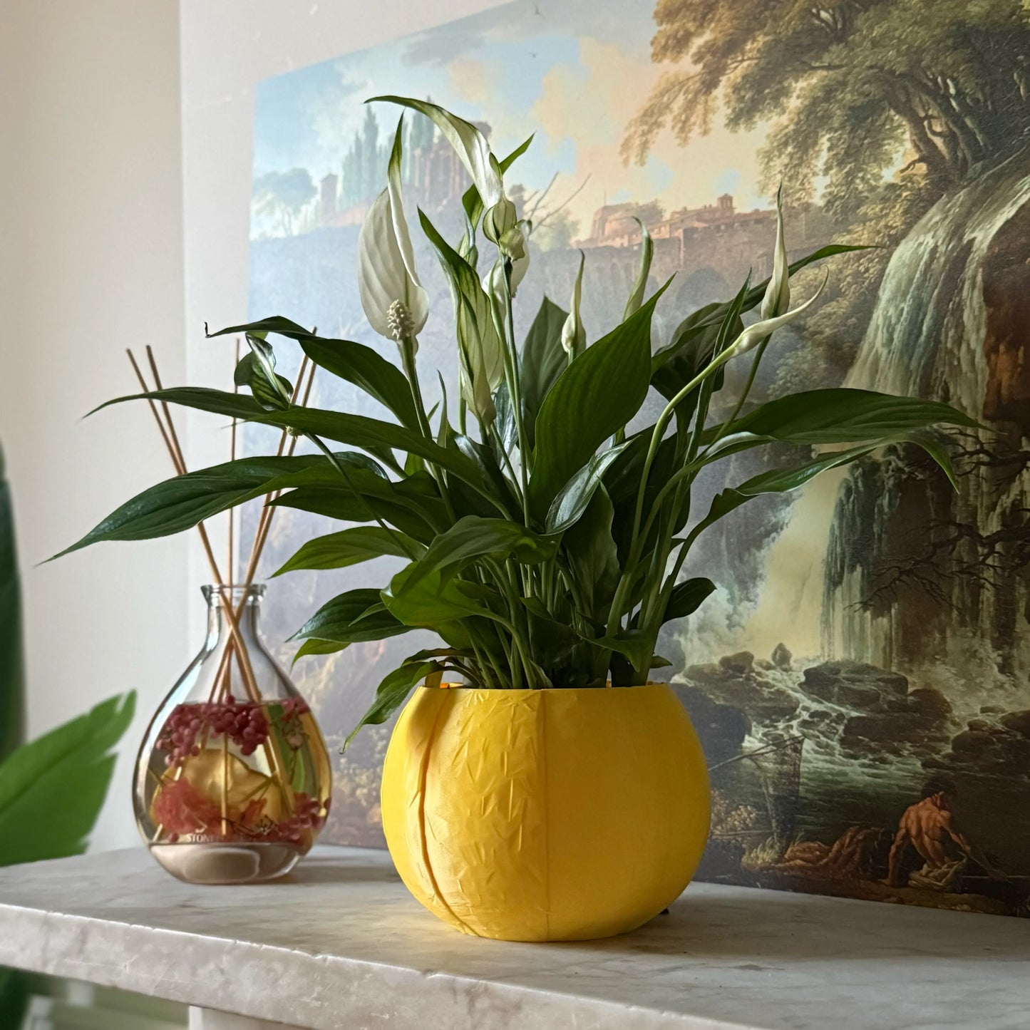 Green potted plant in a yellow plant pot on a marble surface with a painting in the background