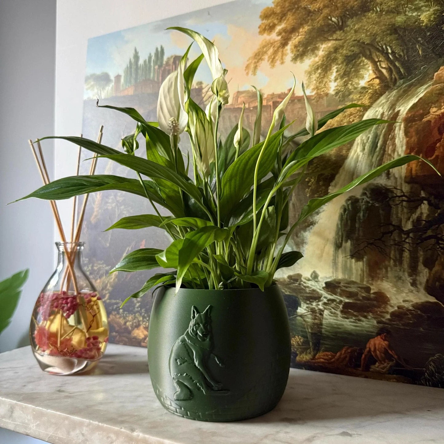 Green potted plant in a white plant pot with an embossed German Shepperd standing on a marble surface
