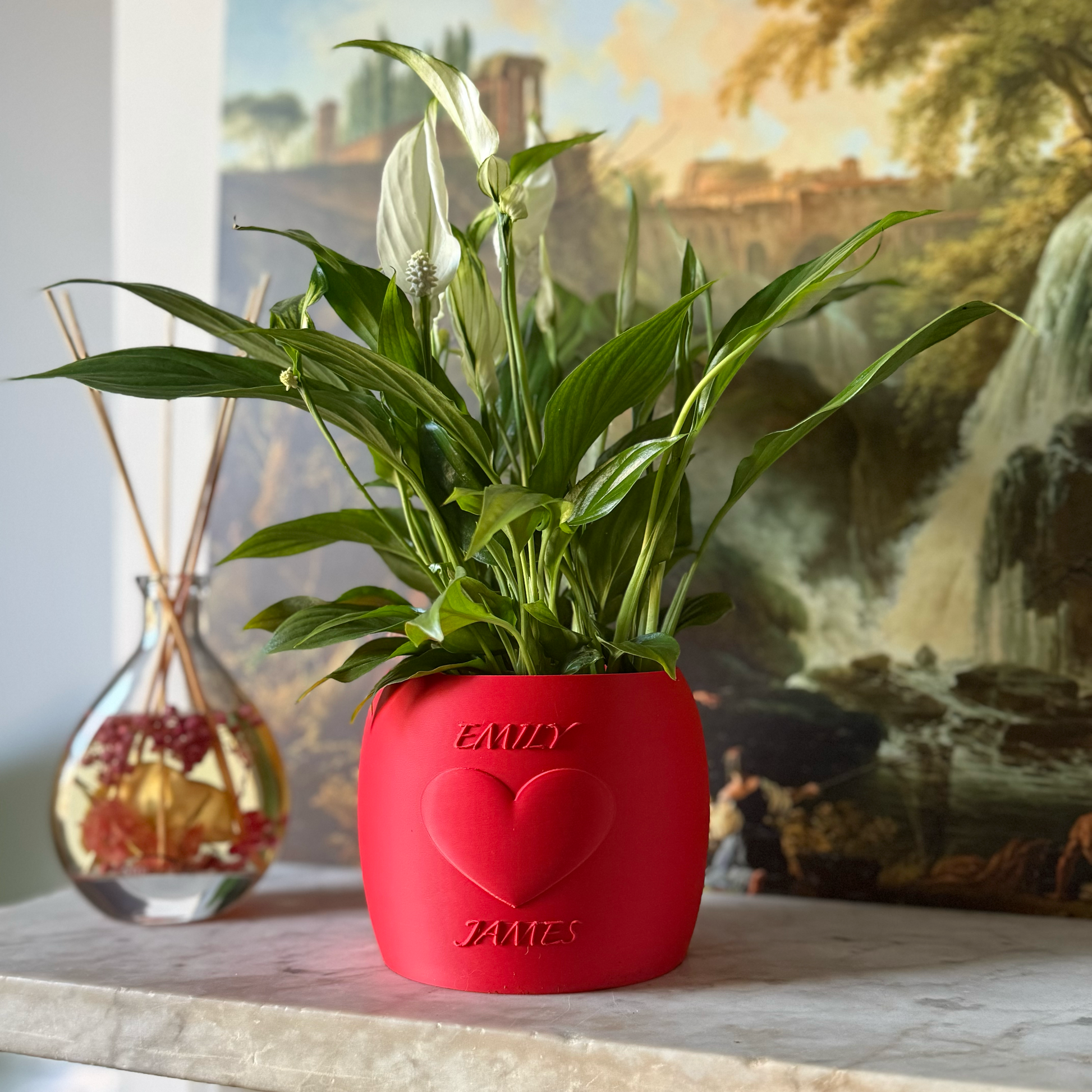 Potted plant in a red Potfolia plant pot with embossed heart and names on a marble surface