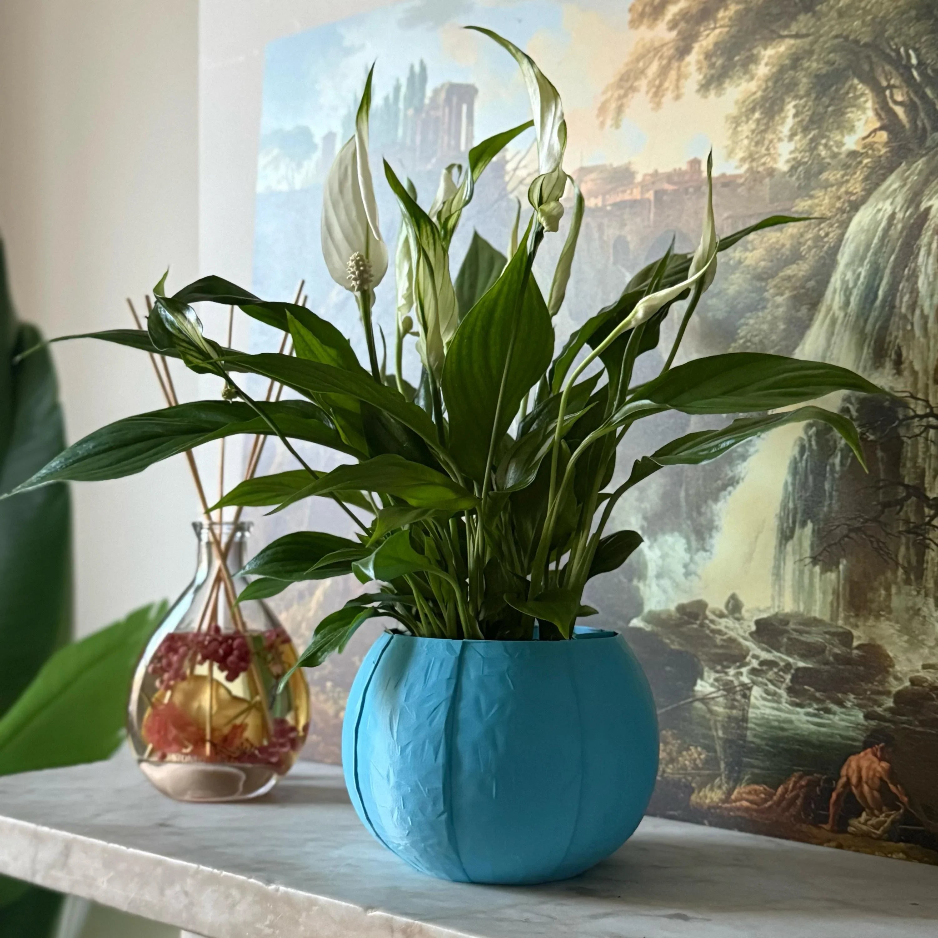 Green potted plant in a blue plant pot on a marble surface with a painting in the background