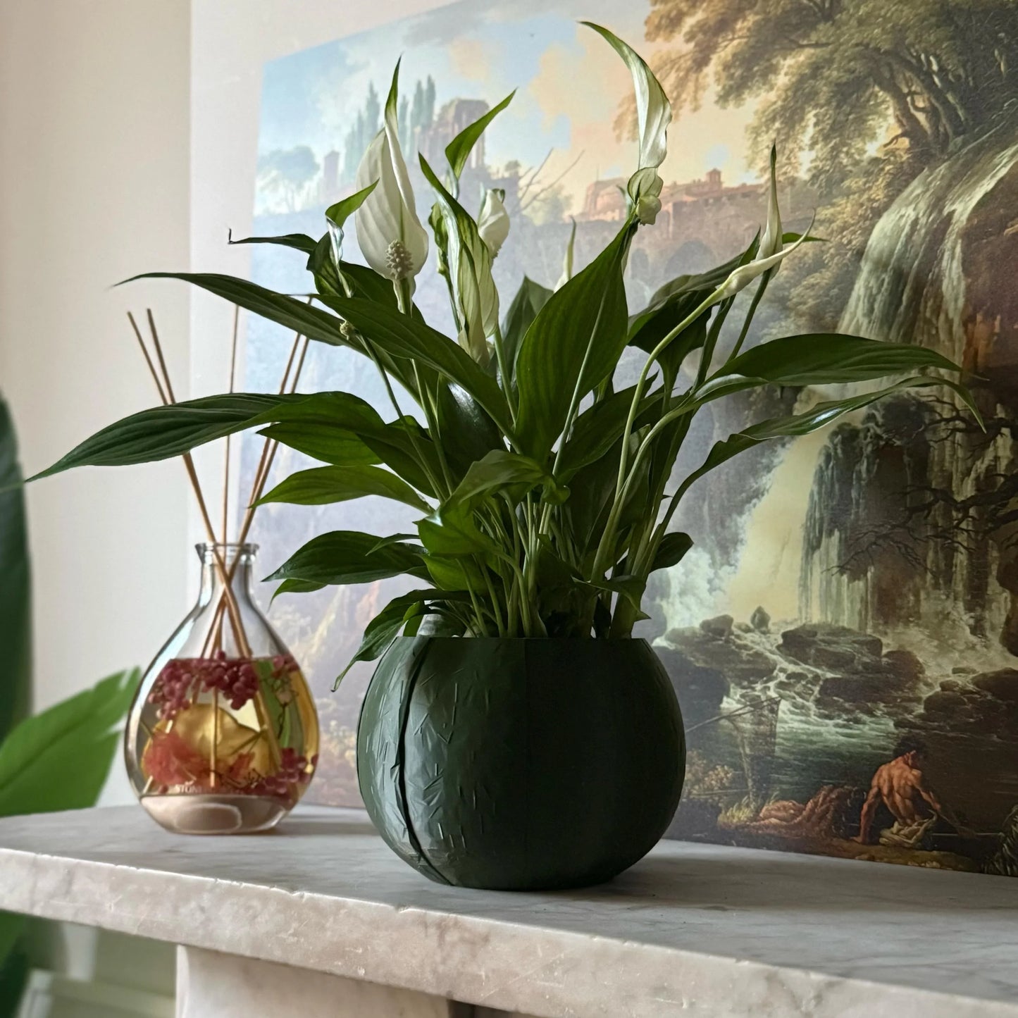 Green potted plant in a green plant pot on a marble surface with a painting in the background