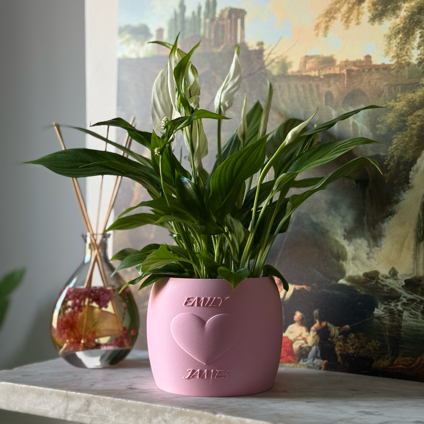 Potted plant in a pink Potfolia plant pot with embossed heart and names on a marble surface