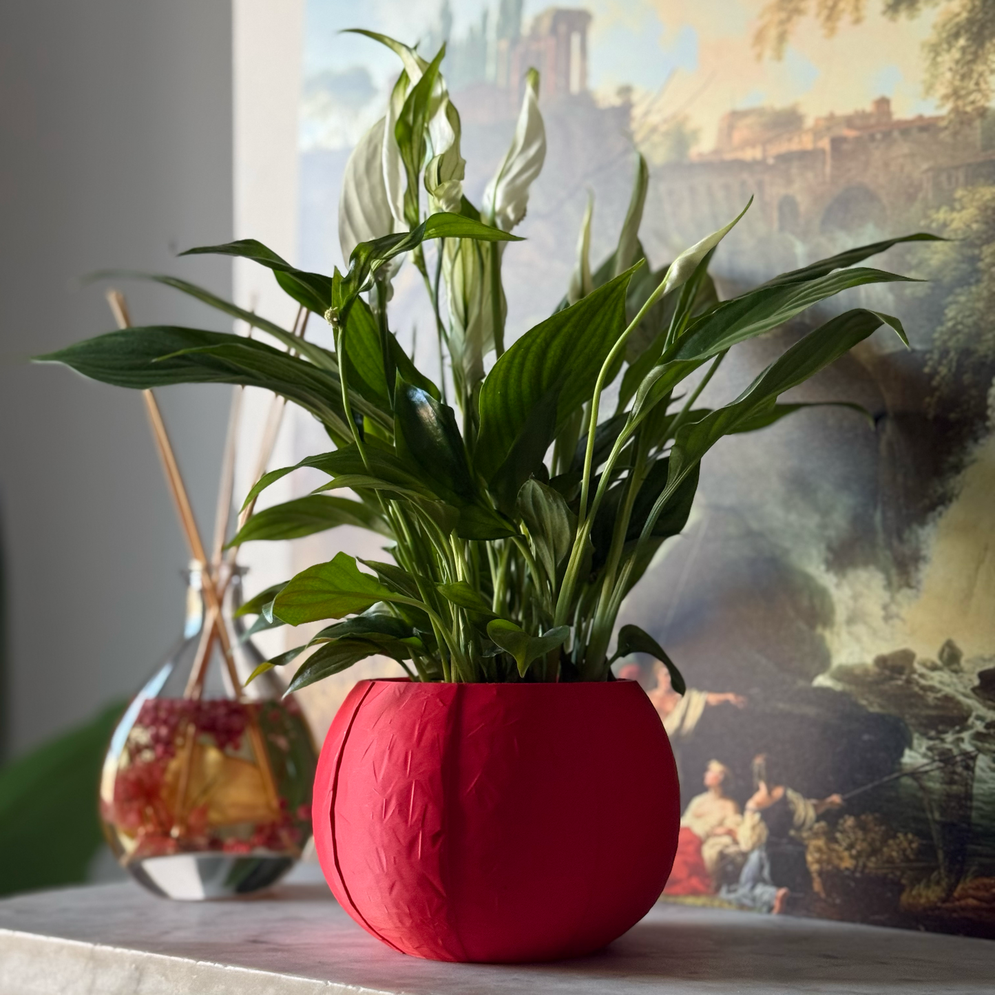 Green potted plant in a red plant pot on a marble surface with a painting in the background