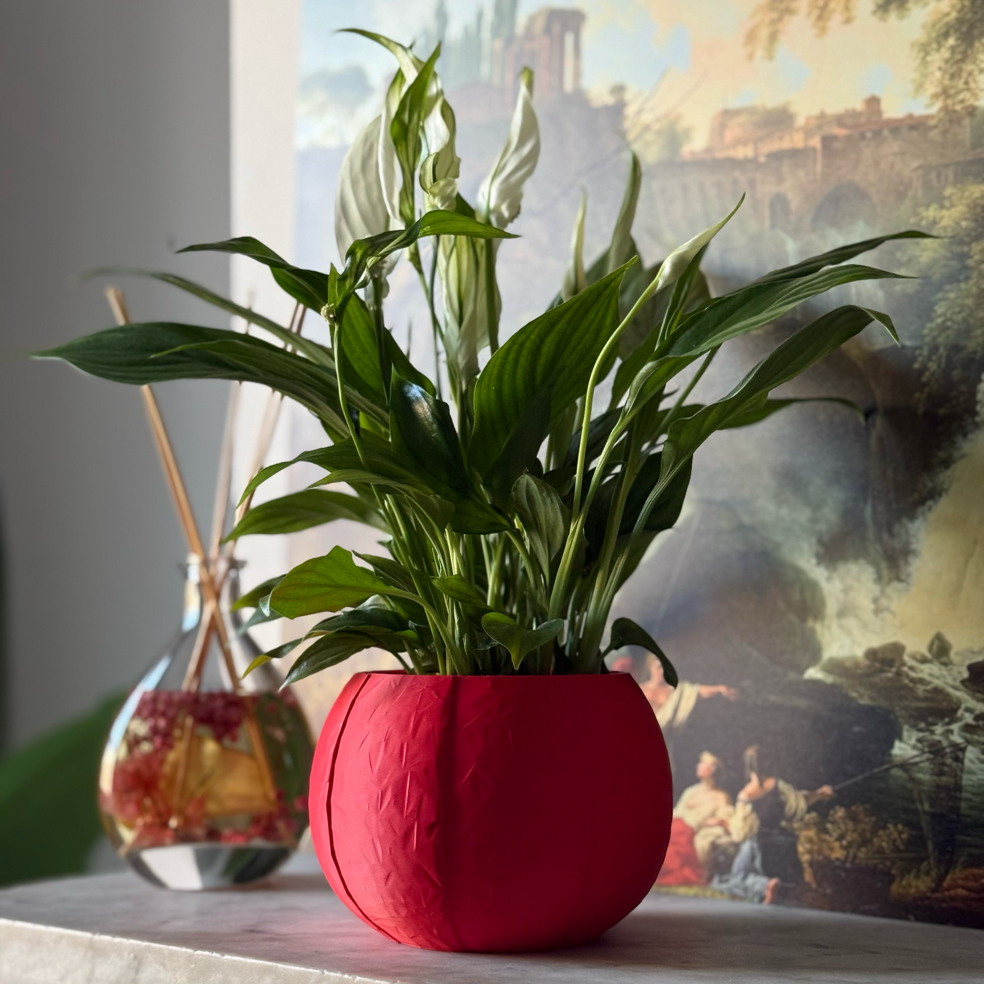 Green potted plant in a red plant pot on a marble surface with a painting in the background