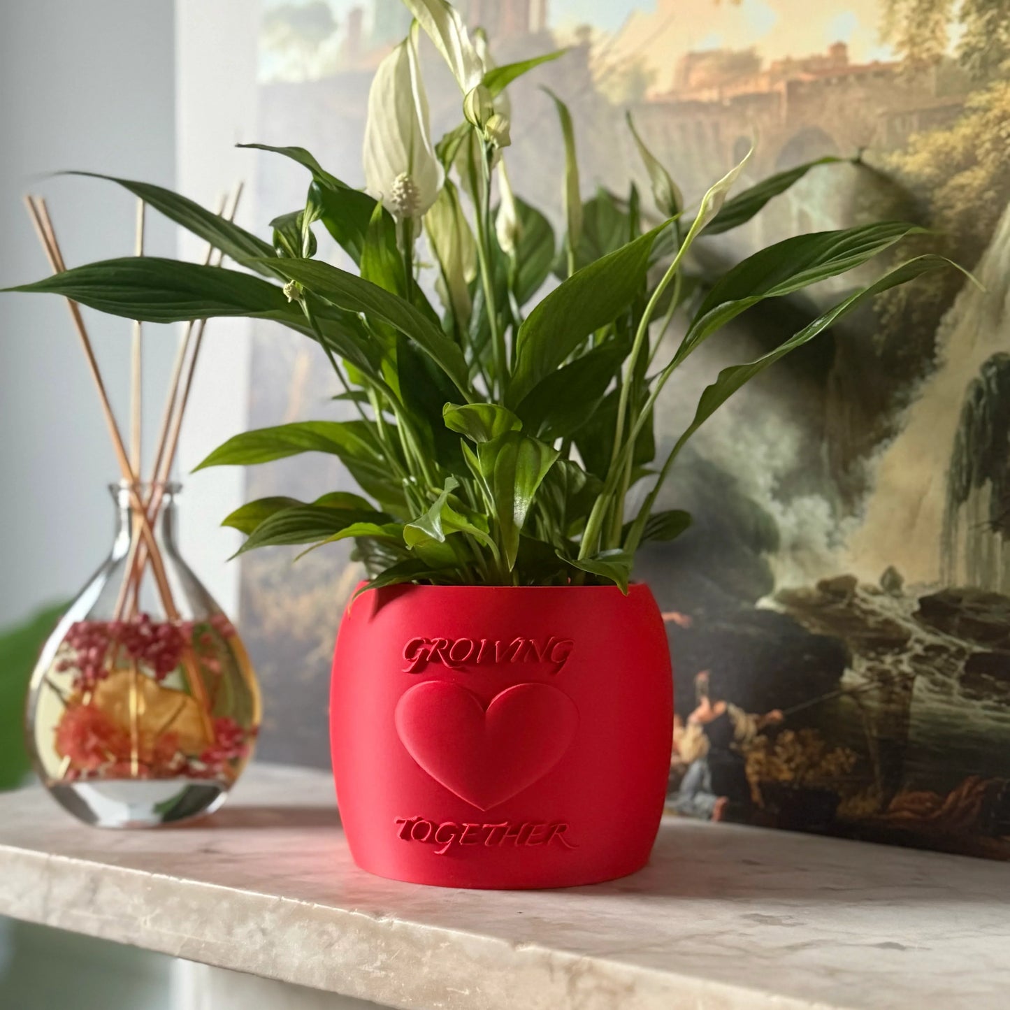 Potted plant in a red Potfolia plant pot with embossed heart and Growing Together text on a marble surface