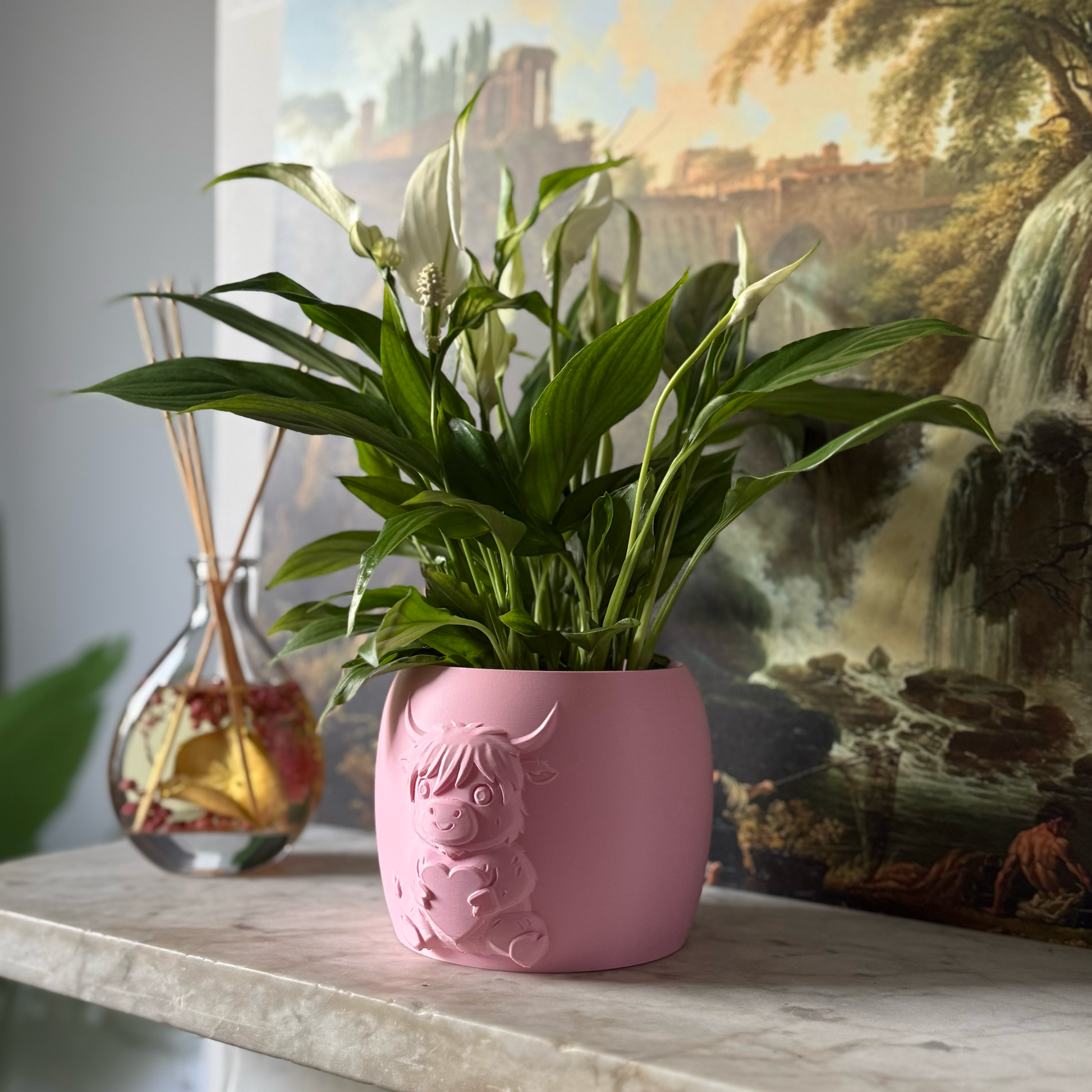 Pink highland cow valentines plant pot with the cow holding a heart in its arms against a painting background on a marble top surface