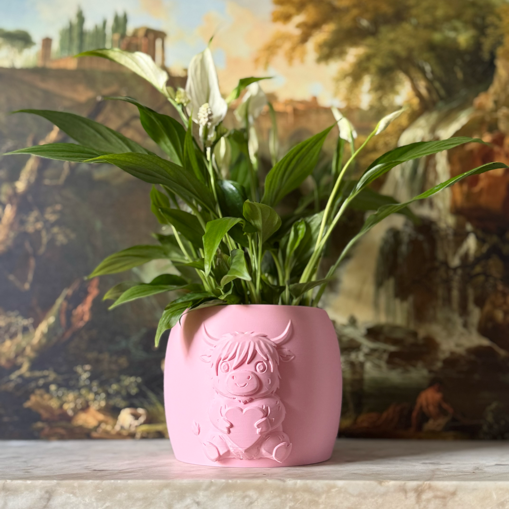 Pink highland cow valentines plant pot with the cow holding a heart in its arms against a painting background on a marble top surface