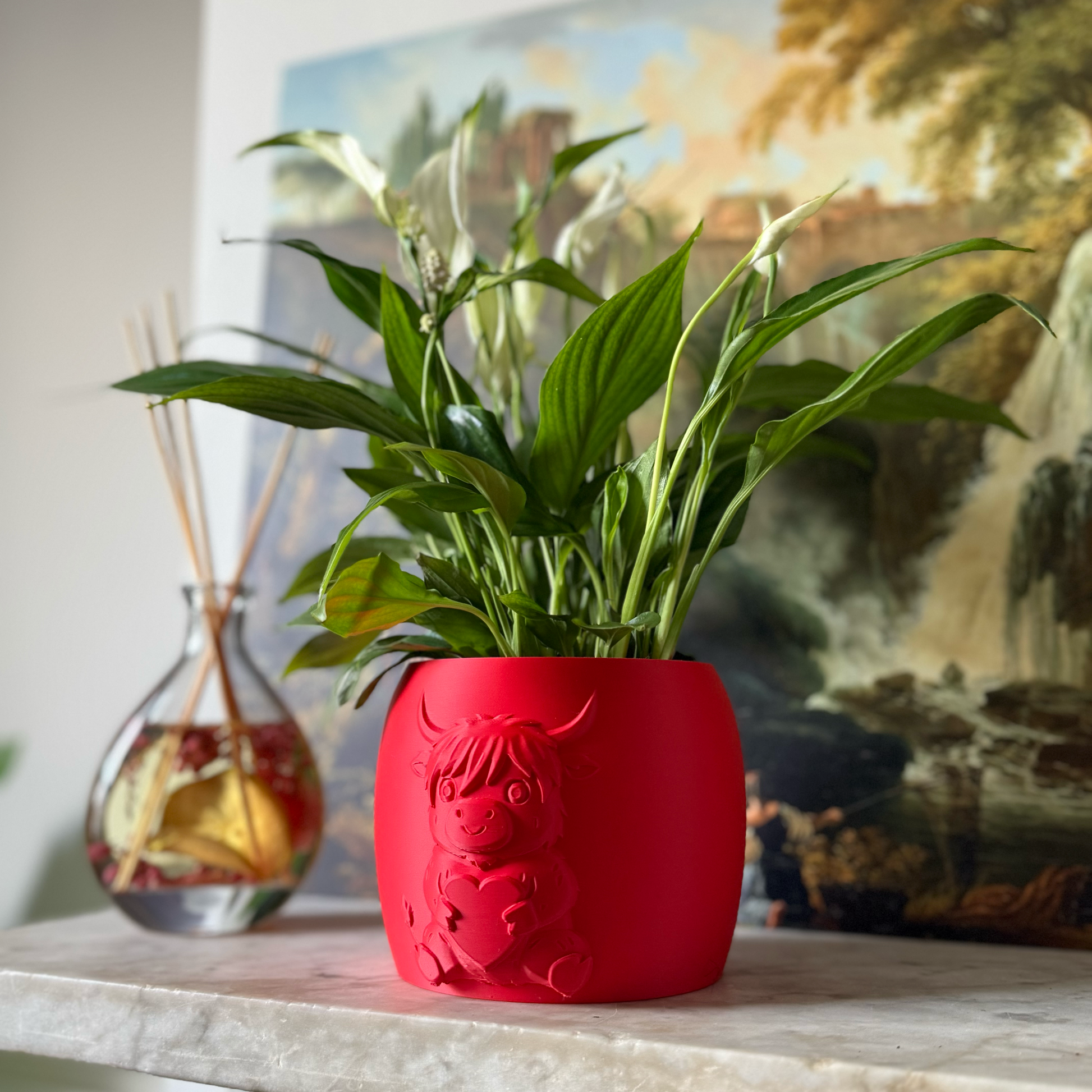 Red highland cow valentines plant pot with the cow holding a heart in its arms against a painting as background on a marble top surface
