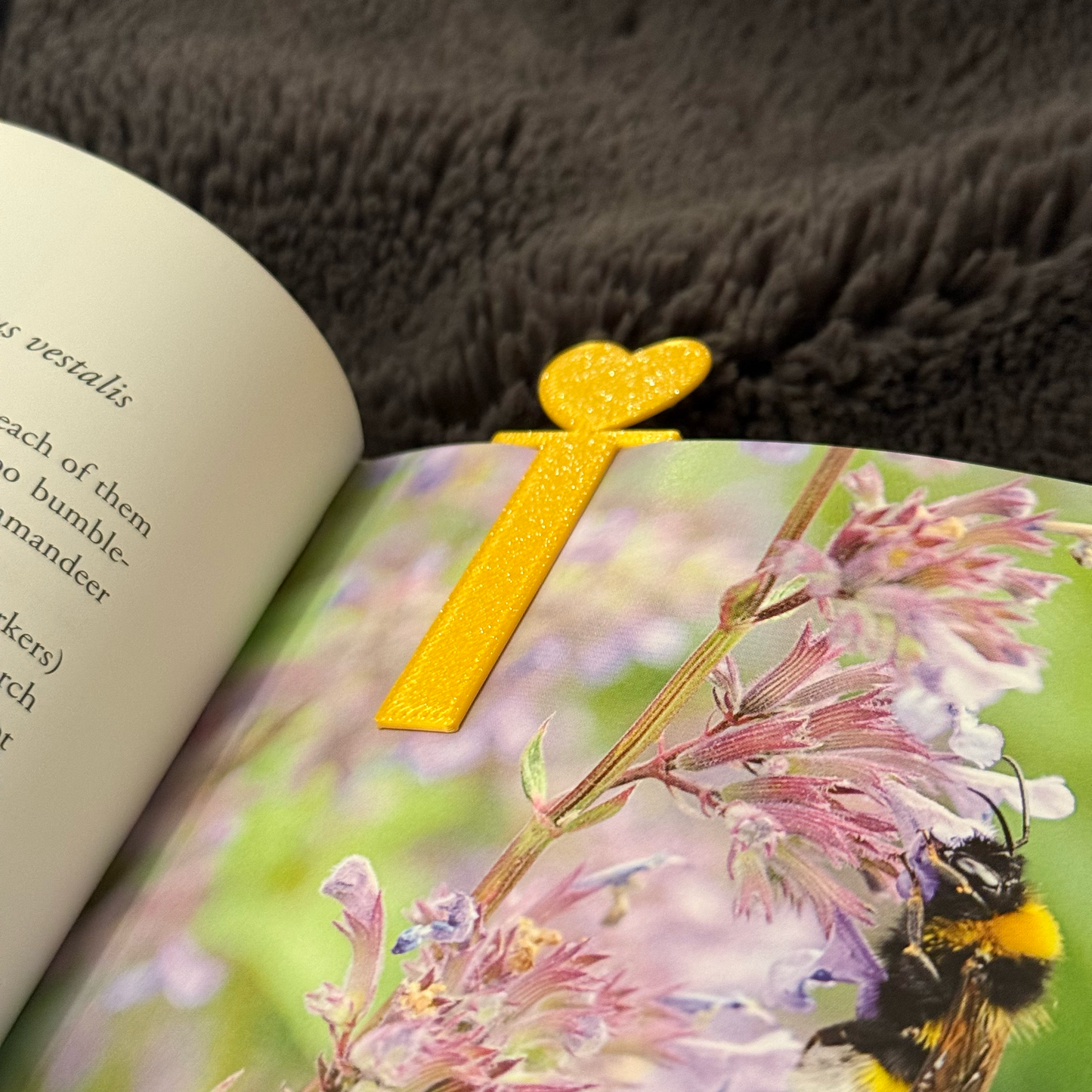 Book with a yellow heart-shaped bookmark on a page featuring a bee and flowers.