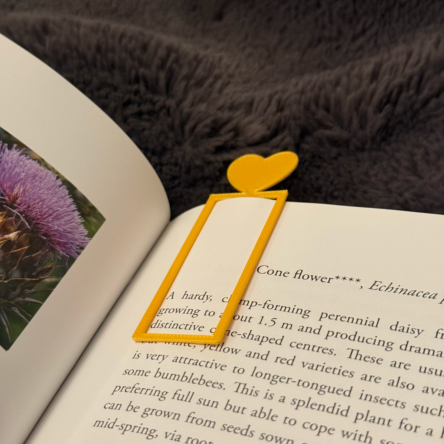 Yellow heart-shaped bookmark on an open book with a purple flower illustration.