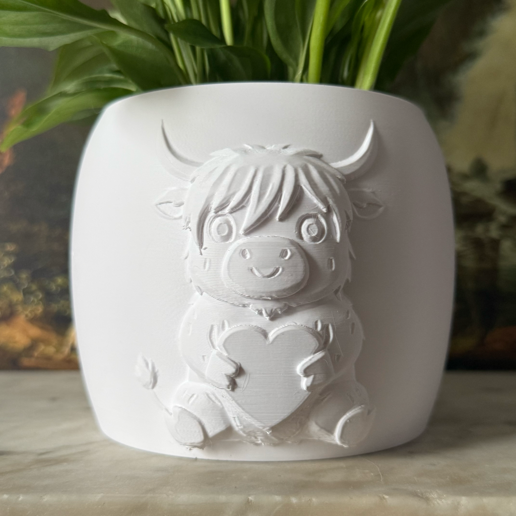 Potted plant in a decorative white highland cow pot on a surface with a scenic painting in the background