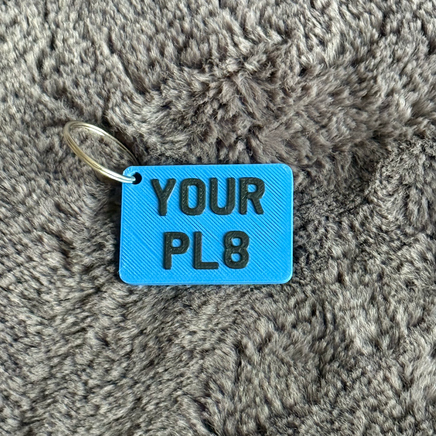Blue square tag with 'YOUR PL8' text on a gray textured surface