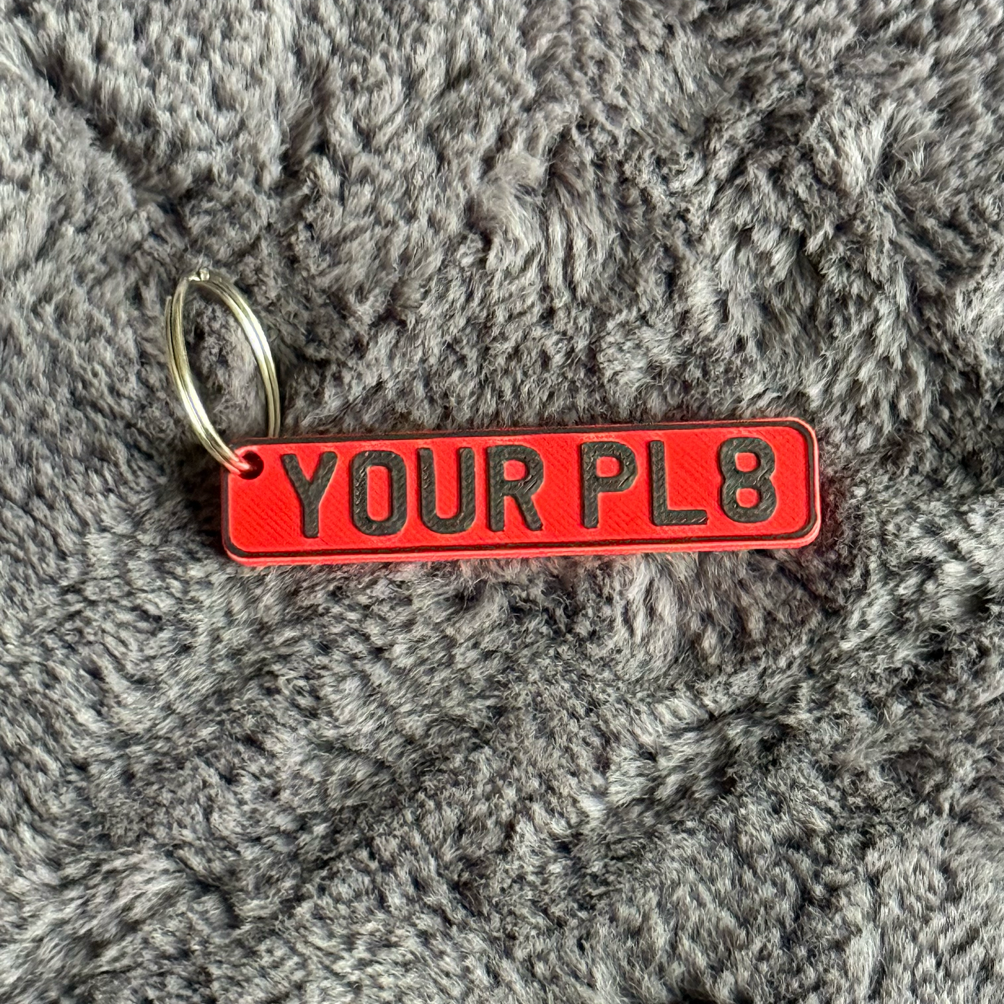 Red keychain with 'YOUR PL8' text on a gray textured surface