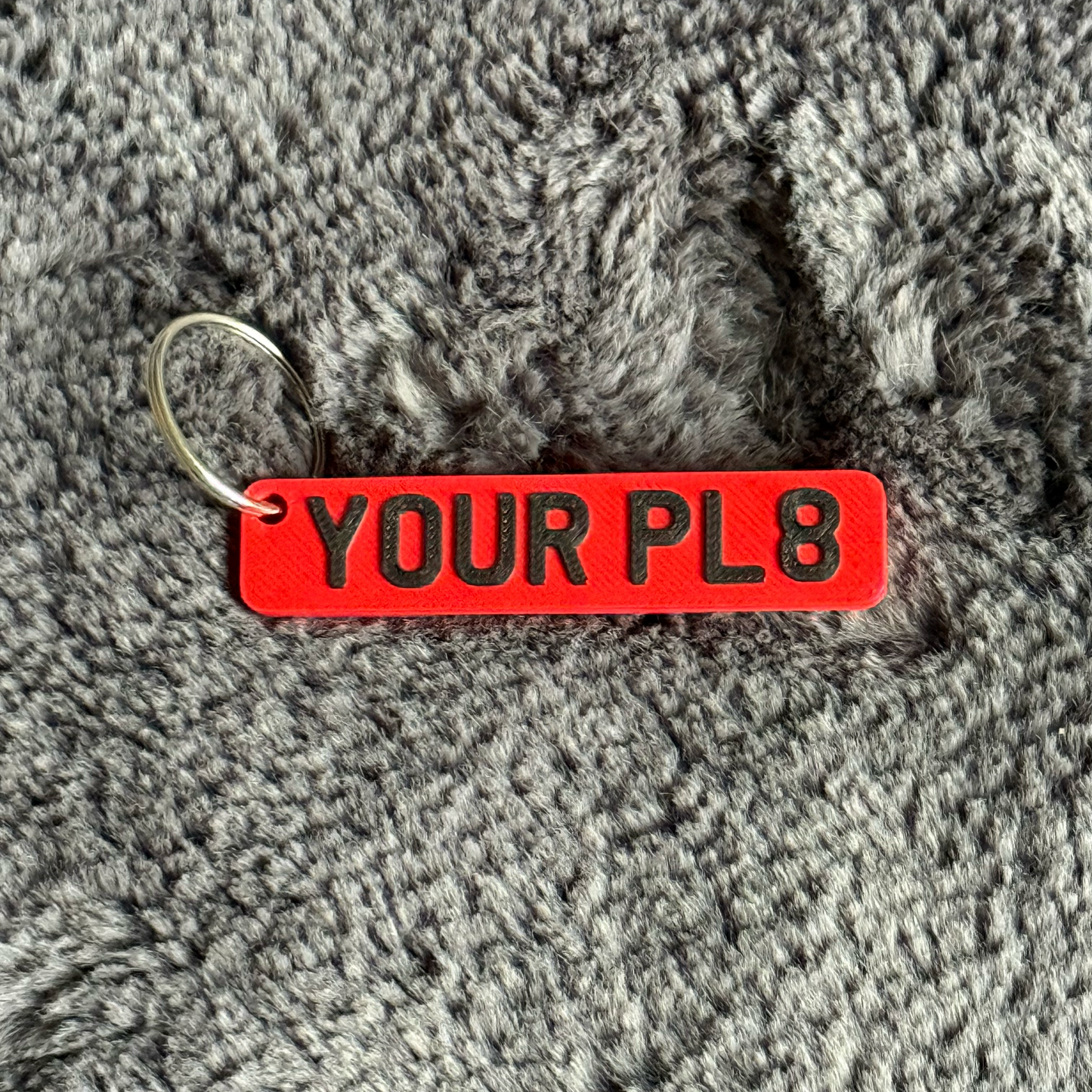 Red keychain with 'YOUR PL8' text on a gray textured surface