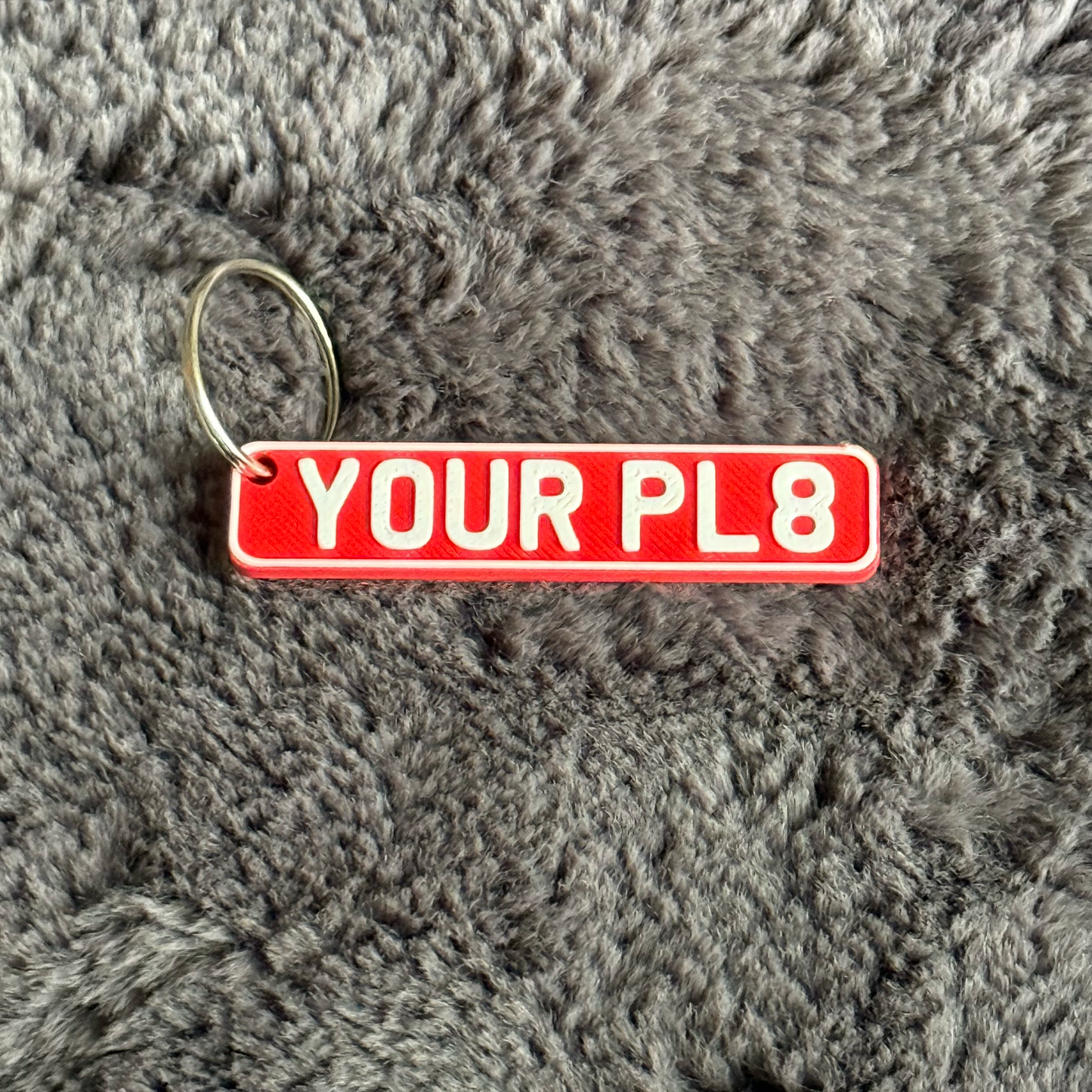 Red keychain with 'YOUR PL8' text on a gray textured surface