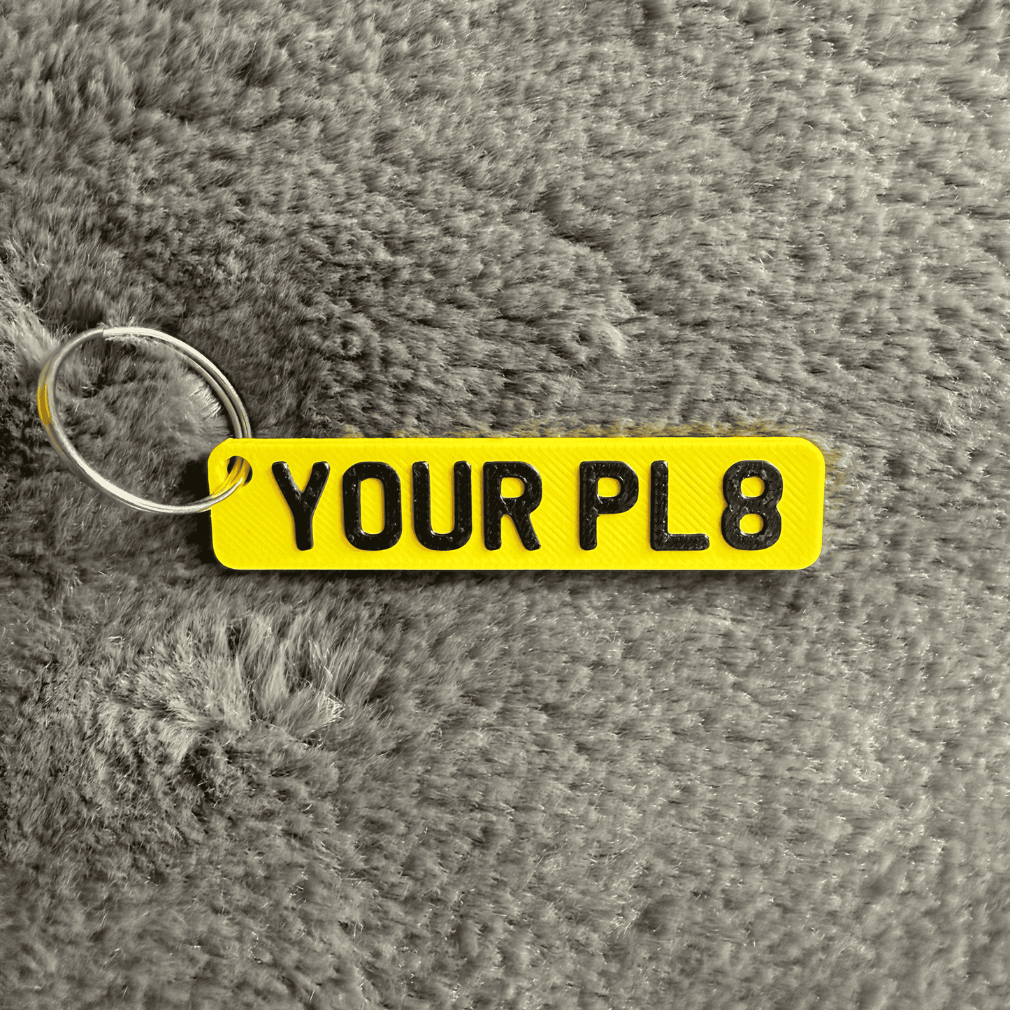 Yellow keychain with 'YOUR PL8' text on a textured gray background